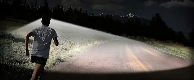 Läufer auf einer dunklen Landstraße mit breitem Lichtkegel der Stirnlampe vor sich